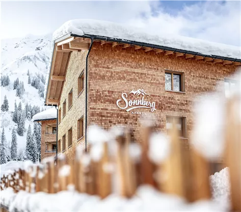 A cozy wooden house in the snow with a clear blue sky in the background. The building belongs to the accommodation "Sonnberg" and is located in a picturesque mountain landscape.