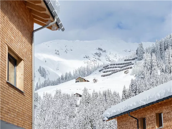 A winter landscape with snow-covered mountains and small huts. The sky is partly cloudy, giving the scene a tranquil atmosphere.