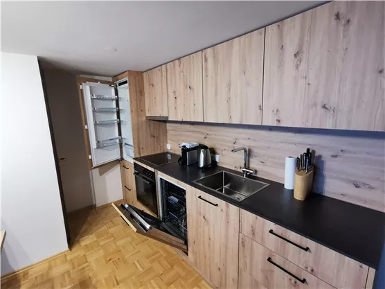 A modern kitchen with wooden fronts and a black work surface. The refrigerator is open and the kitchen appliances are neatly arranged.