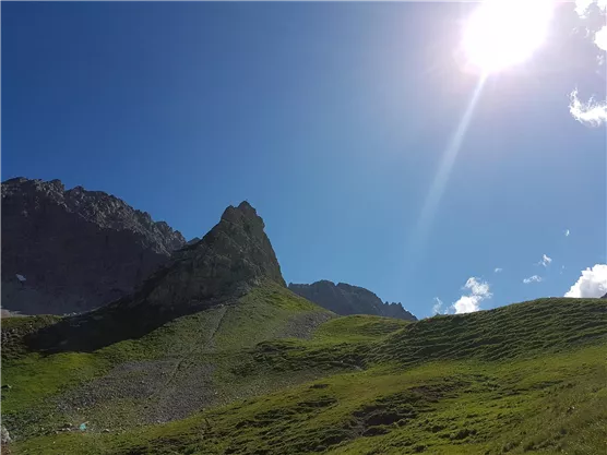 A picturesque mountain with green meadows and a bright blue sky. The sun shines brightly and entices exploration of nature.