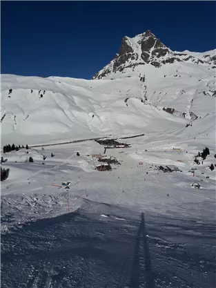 A snow-covered landscape with a mountain in the background. In the foreground, ski lifts and a small cabin are visible.