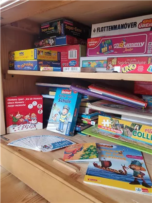 A wooden shelf full of board games and learning materials. On the lower level are various games and books inviting play and learning.