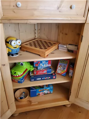 A wooden shelf with various games and toys.
At the top is a minion and in the middle lies a chessboard.