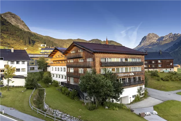 An impressive building in the mountains with a beautiful garden. The surroundings showcase tall mountains and a clear, blue sky.