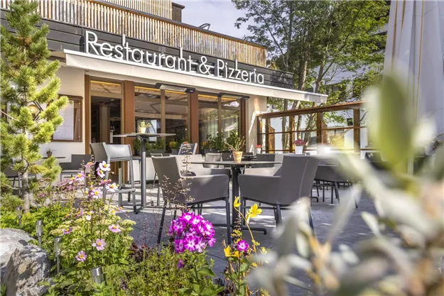 An inviting restaurant with an outdoor area and tables. Colorful flowers surround the terrace, which invites guests to linger.