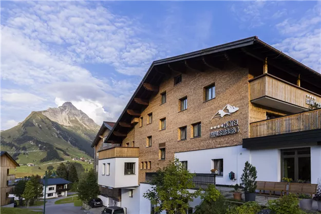 A cozy chalet in the mountains with a clear blue sky. In the background, majestic mountains can be seen.