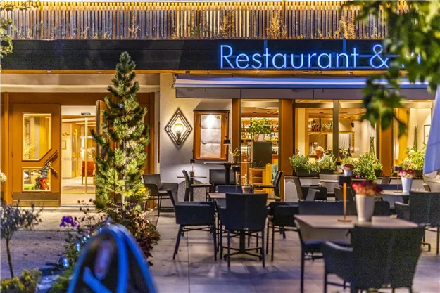 A cozy restaurant with an outdoor area and many tables. The lighting creates an inviting atmosphere.