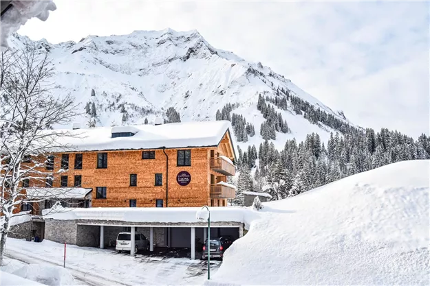 Ein wunderschönes Bergpanorama mit schneebedeckten Gipfeln. Im Vordergrund steht ein Holzgebäude, umgeben von viel Schnee.