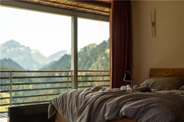 A cozy bedroom with a bed and a view of the mountains. Large windows offer a view of the green mountain landscape.