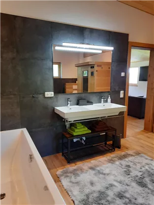 A modern bathroom with a large bathtub and an elegant sink. The walls are in a dark gray, and there is a large mirror above the sink.