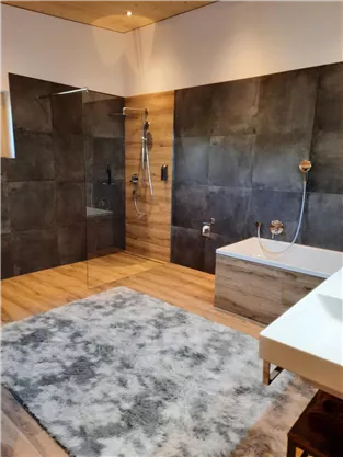 A modern bathroom with a large shower and a bathtub. The floor is made of wood and a soft rug lies in the room.