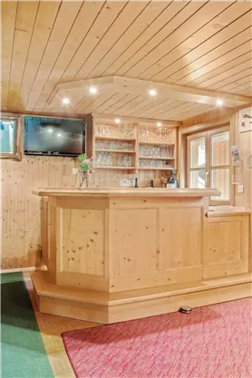 Eine gemütliche Holzbar mit einem hellen Innenraum. Im Hintergrund sind ein Fernseher und Regale mit Gläsern zu sehen.