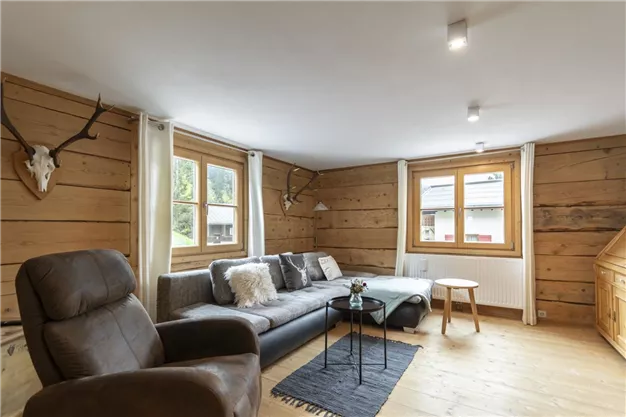 A cozy living room with wooden walls and modern furniture. A gray sofa and a small table create an inviting atmosphere.