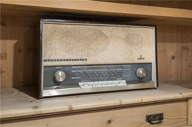 A vintage radio on a wooden shelf. The device has a classic look with rotating knobs and an audible material.