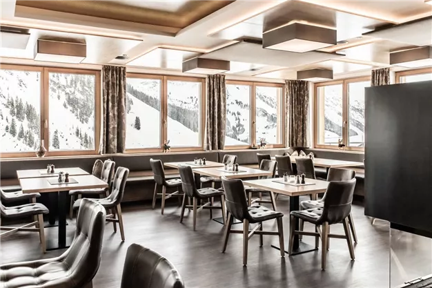 A modern restaurant with elegant tables and chairs. Large windows offer a view of snow-capped mountains.