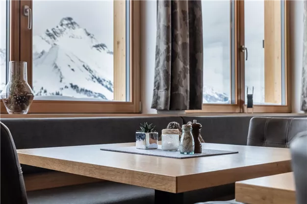 A cozy table with spices and plants, in front of a window with a view of snow-covered mountains. The atmosphere is warm and inviting.