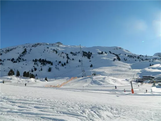 A snowy mountain landscape with blue skies. Skiers enjoy the slopes and the sunny winter atmosphere.