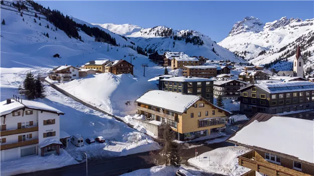 A picturesque mountain landscape with snow-covered hills and cozy chalets. The clear blue sky complements the winter idyll.