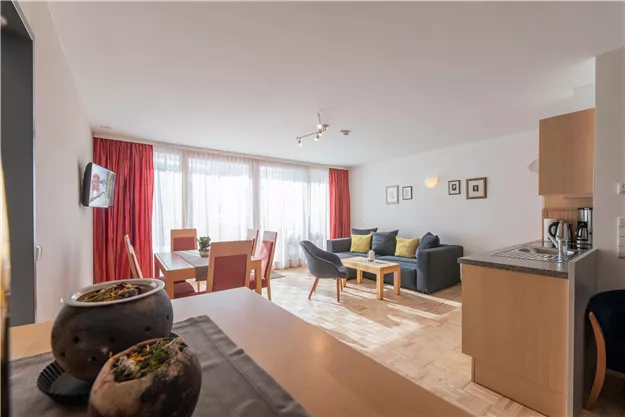 A modern living and dining room with a cozy sofa and a dining table. Large windows provide plenty of daylight and an inviting atmosphere.
