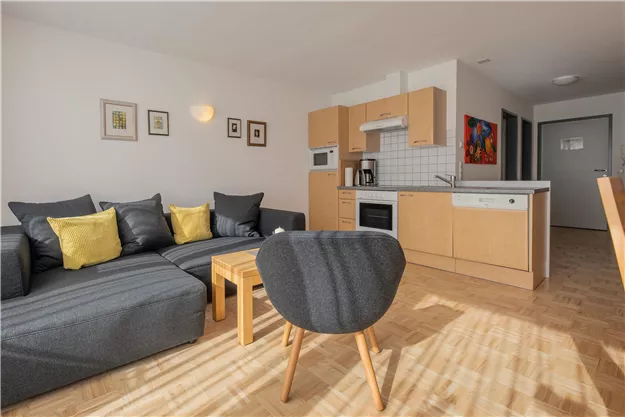 A modern apartment with a cozy sofa and a dining table. The kitchen is well equipped, and the room has many windows for natural light.