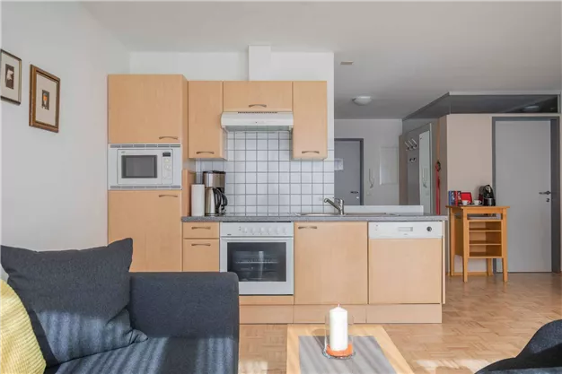 A modern kitchen corner with wooden cabinets and appliances. The room is bright and inviting, with a cozy living area.