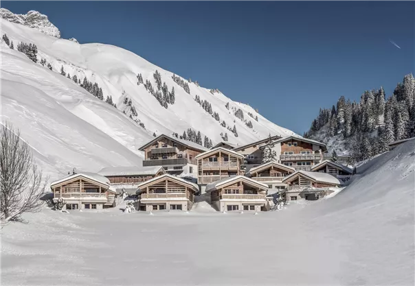 Eine malerische Winterlandschaft mit schneebedeckten Hügeln und modernen Chalets. Der klare Himmel lässt die frostige Atmosphäre strahlen.