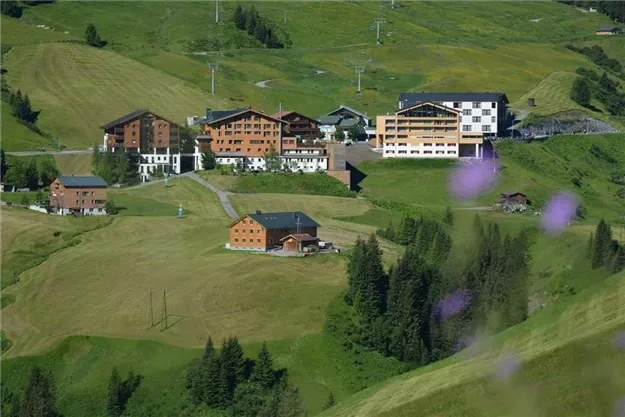 A picturesque mountain landscape with several buildings and green grass. The surroundings are calm and inviting, ideal for a relaxing holiday.