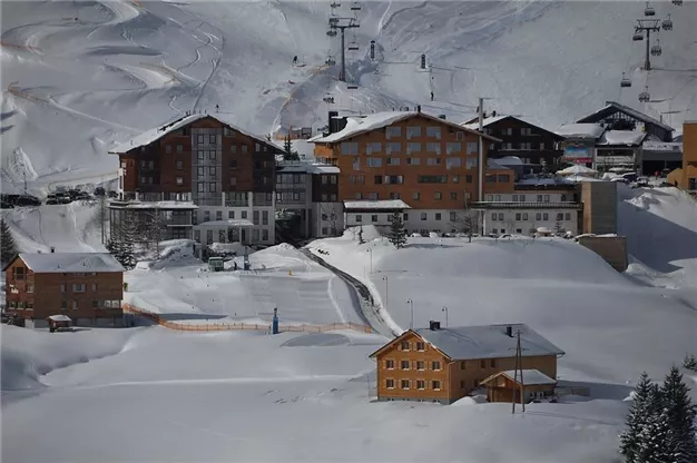 A picturesque mountain village in the snow, surrounded by snow-covered hills. The buildings are typical of alpine architecture and convey a cozy atmosphere.