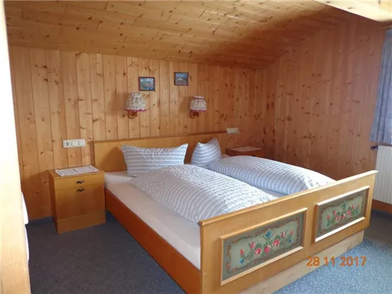 Ein gemütliches Schlafzimmer mit Holzwänden und einem Doppelbett. Neben dem Bett steht ein Nachttisch und es gibt dekorative Lampen an den Wänden.