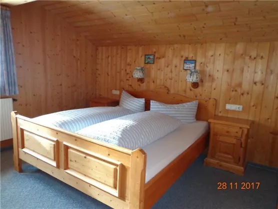 Ein gemütliches Schlafzimmer mit einem Holzbett und zwei Nachttischen. Die Wände sind aus Holz, und es gibt zwei kleine Bilder an der Wand.