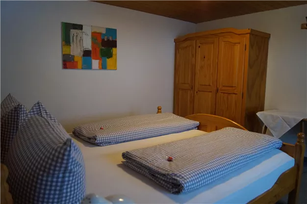 A cozy bedroom with two beds, adorned with checkered comforters and pillows. Wooden bedroom furniture and a colorful painting complete the space.