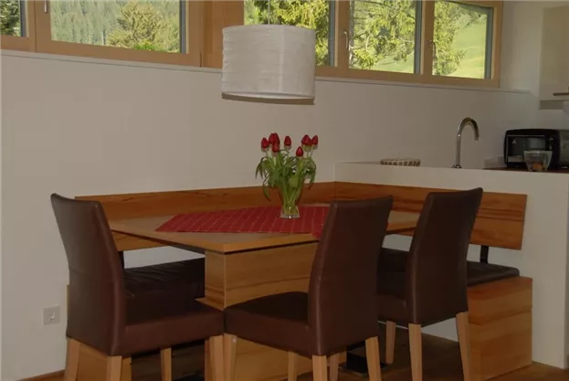 A dining area with a wooden table and brown chairs. On the table is a vase with red flowers.