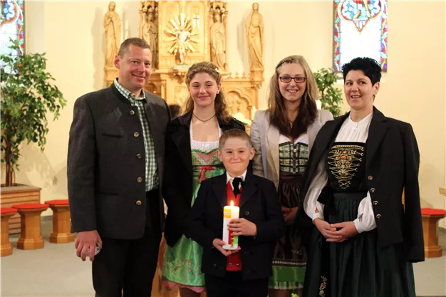 A group of five people is standing in a church. They are wearing traditional costumes, and the boy is holding a candle in his hand.