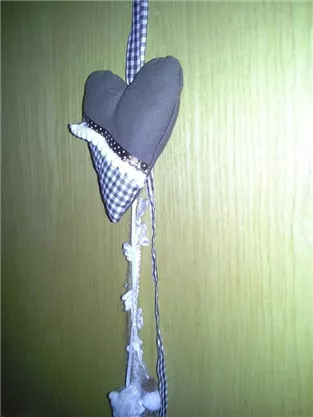 A hanging fabric heart with a checkered pattern and a decorative row of beads. Below it, several white flowers and pompons are hanging.