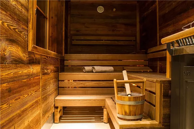 A cozy wooden sauna with benches, a bucket, and a towel. The room exudes a relaxing atmosphere.