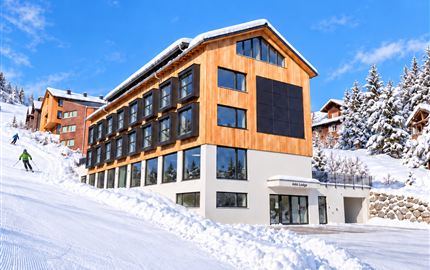 Ein modernes Hotel in einer schneebedeckten Landschaft. Der Himmel ist blau und die Piste ist gut präpariert.
