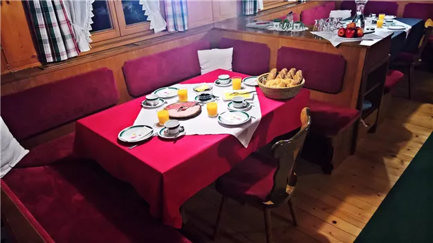 Ein einladender Frühstückstisch mit roter Tischdecke. Auf dem Tisch sind Teller, Tassen, Croissants und Säfte angerichtet.