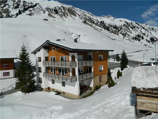 A multi-story building in a snowy landscape. In the background, there are mountains and a clear blue sky.
