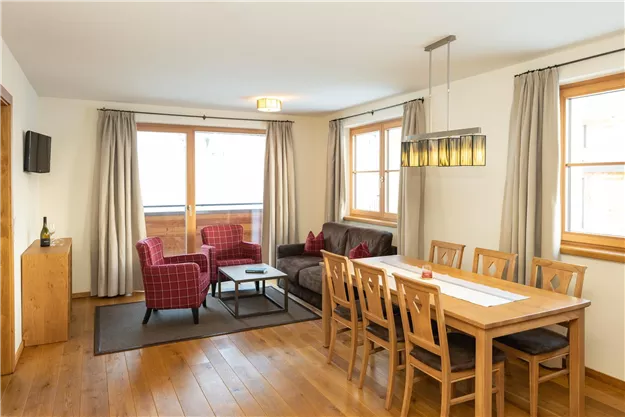 A cozy living room with a dining table and modern furniture. Bright windows let in plenty of daylight and create a friendly atmosphere.