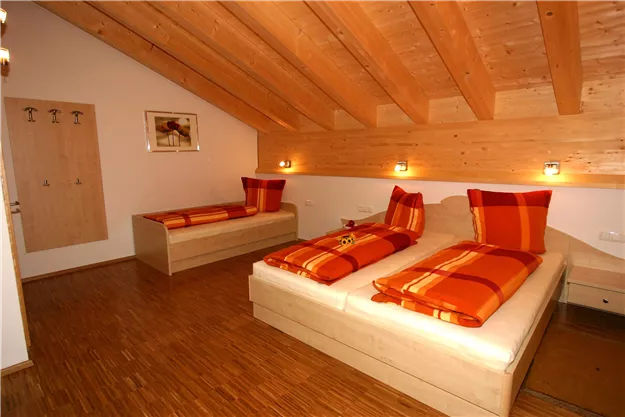 A cozy bedroom with two beds and a wooden ceiling. The pillows are in shades of orange.