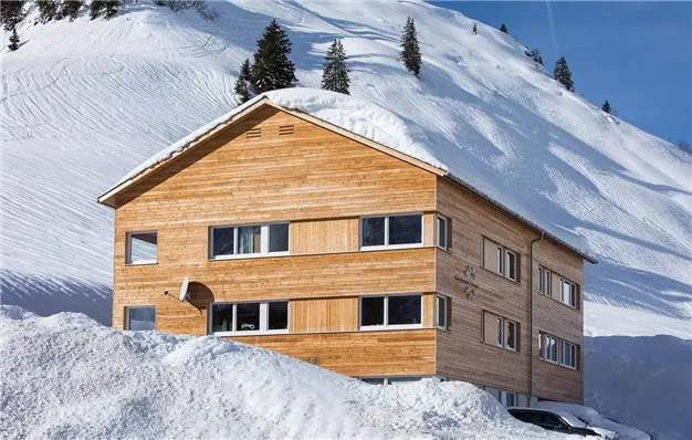Ein Holzhaus in einer verschneiten Landschaft. Im Hintergrund sind schneebedeckte Hügel zu sehen.