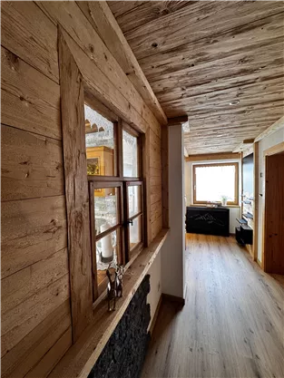 Ein gemütlicher Flur mit Holzwänden und einem Holzdecken. Durch die Fenster fällt natürliches Licht in den Raum.