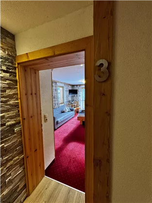 A glimpse into a cozy room with a red carpet and light furniture. The door with the number 3 leads into the room.