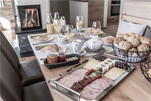 Ein schön gedeckter Tisch mit einer Auswahl an Frühstückslebensmitteln und Getränken. Im Hintergrund brennt ein Kamin.