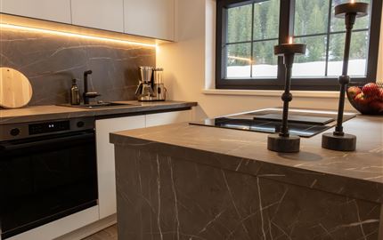 Moderne Küche mit grauem Marmor und eleganter Beleuchtung. Es gibt einen Herd, einen Backofen und dekorative Kerzenhalter.