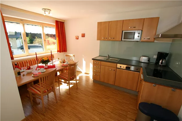 A modern kitchen with light wooden furniture and a dining table. The window provides plenty of daylight and an inviting atmosphere.