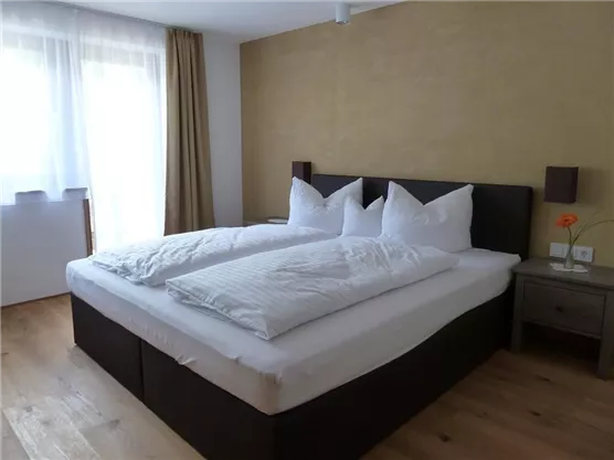A cozy bedroom with a large double bed and white bedspreads. The windows let in plenty of daylight and create a bright, welcoming atmosphere.