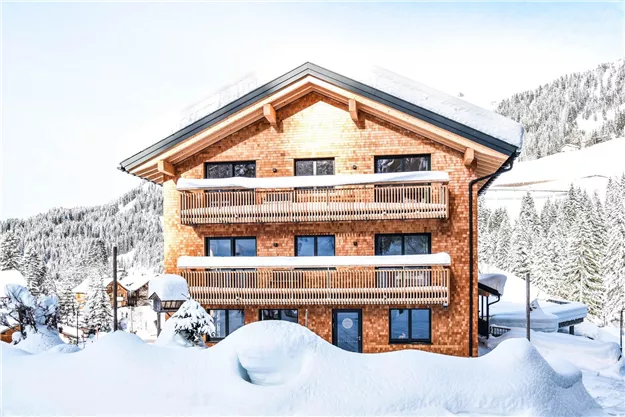 Ein schönes Holzhaus im Winter, umgeben von Schnee. Die Balkone bieten einen Blick auf die verschneiten Berge.