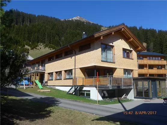 A modern two-story building amidst a green landscape. In the background, mountains and trees can be seen.