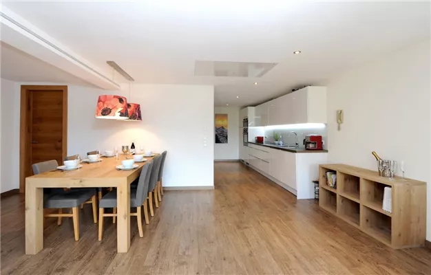A modern dining area with a large wooden table and chairs. The open kitchen is bright and inviting, with clean lines and modern appliances.